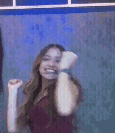A Woman Is Smiling And Dancing In Front Of A Blue Wall . GIF