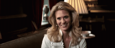 A Woman Is Smiling And Holding A Cup Of Coffee And The Word Emma Is On The Bottom Of Her Shirt . GIF