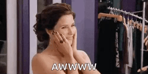 A Woman Is Smiling And Holding Her Face In Front Of A Clothes Rack In A Store . GIF