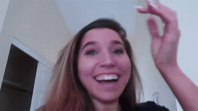 A Woman Is Smiling And Holding Her Hand Up In The Air While Looking At The Camera . GIF