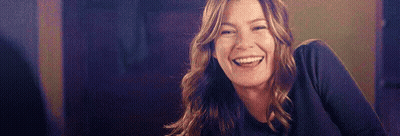 A Woman Is Smiling And Laughing While Sitting At A Table In A Dark Room . GIF