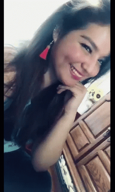 A Woman Is Smiling And Looking At The Camera While Sitting In Front Of A Wooden Cabinet . GIF