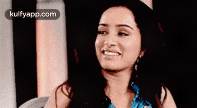 A Woman Is Smiling And Looking At The Camera While Sitting On A Chair . GIF