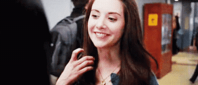 A Woman Is Smiling And Looking At The Camera While Standing In A Hallway . GIF