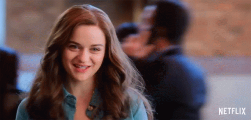 A Woman Is Smiling And Looking At The Camera While Standing In Front Of A Man . GIF