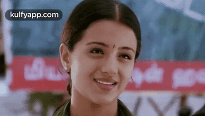 A Woman Is Smiling And Looking At The Camera While Standing In Front Of A Sign . GIF