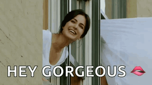 A Woman Is Smiling And Looking Out Of A Window With The Words `` Hey Gorgeous '' Written Below Her . GIF
