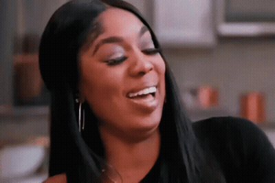 A Woman Is Smiling And Making A Funny Face While Wearing A Black Shirt And Earrings . GIF