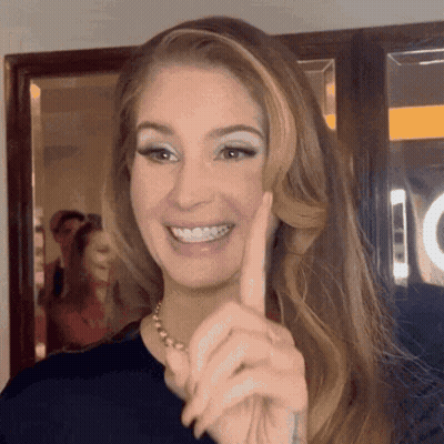 A Woman Is Smiling And Pointing At The Camera With Her Finger . GIF