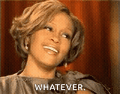 A Woman Is Smiling And Saying `` Whatever '' While Sitting In Front Of A Red Curtain . GIF