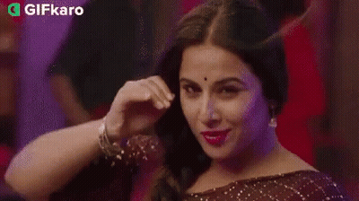 A Woman Is Smiling And Touching Her Hair In A Braid . GIF