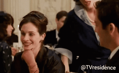 A Woman Is Smiling At A Man While Sitting At A Table In A Crowded Room . GIF