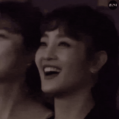 A Woman Is Smiling In A Black And White Photo . GIF