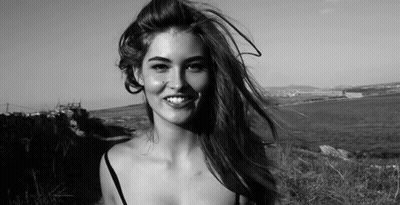 A Woman Is Smiling In A Black And White Photo While Her Hair Is Blowing In The Wind . GIF