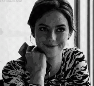 A Woman Is Smiling In A Black And White Photo While Holding A Cell Phone . GIF