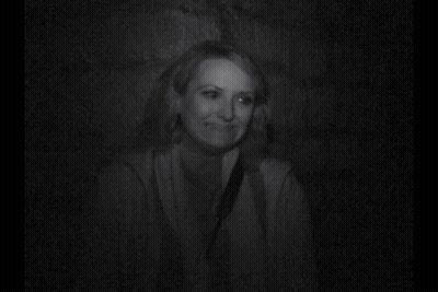 A Woman Is Smiling In A Black And White Photo While Sitting In A Dark Room . GIF