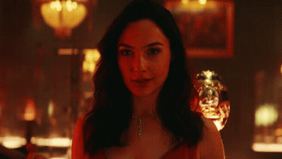 A Woman Is Smiling In A Dark Room With A Glass In The Background GIF