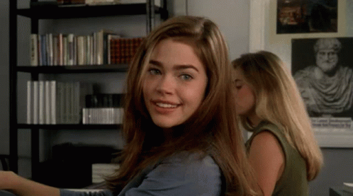 A Woman Is Smiling In Front Of A Bookshelf With A Picture Of A Man On It GIF