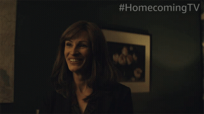 A Woman Is Smiling In Front Of A Framed Picture With #Homecomingtv Written On The Bottom GIF