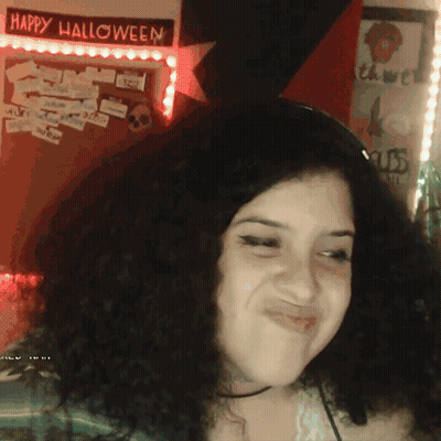 A Woman Is Smiling In Front Of A Happy Halloween Sign GIF