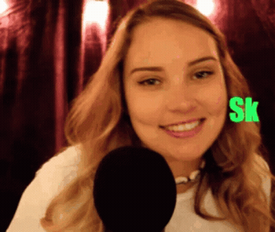 A Woman Is Smiling In Front Of A Microphone With The Letters Sk On Her Face GIF