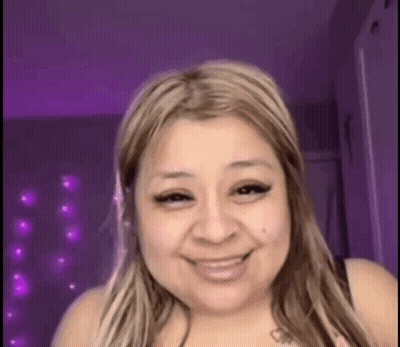 A Woman Is Smiling In Front Of A Purple Wall And Purple Lights . GIF