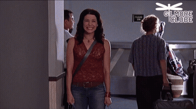 A Woman Is Smiling In Front Of A Sign That Says " Gilmore Club " GIF