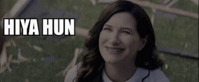 A Woman Is Smiling In Front Of A Sign That Says " Hiya Hun " GIF