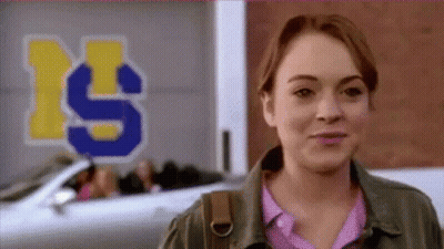 A Woman Is Smiling In Front Of A Sign That Says ' S ' On It . GIF