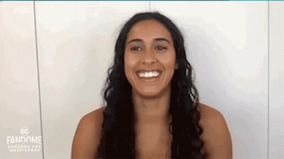 A Woman Is Smiling In Front Of A White Wall . GIF