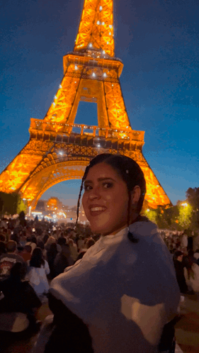 A Woman Is Smiling In Front Of The Eiffel Tower At Night GIF