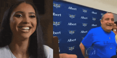 A Woman Is Smiling Next To A Man In Front Of A Wall With Albert Written On It GIF