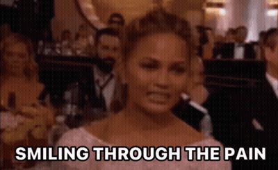 A Woman Is Smiling Through The Pain While Sitting In Front Of A Crowd . GIF