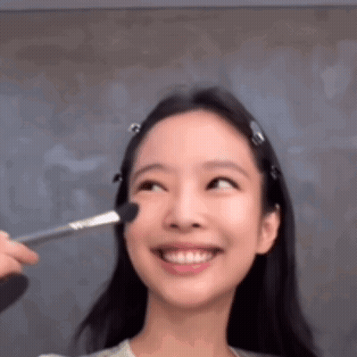 A Woman Is Smiling While Getting Her Makeup Done With A Brush On Her Face . GIF