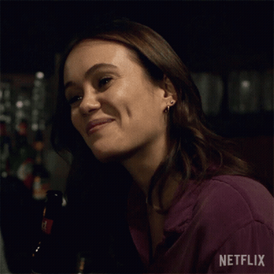 A Woman Is Smiling While Holding A Bottle Of Beer In A Bar . GIF
