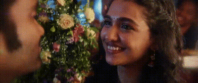 A Woman Is Smiling While Holding A Bouquet Of Flowers In Front Of A Man . GIF