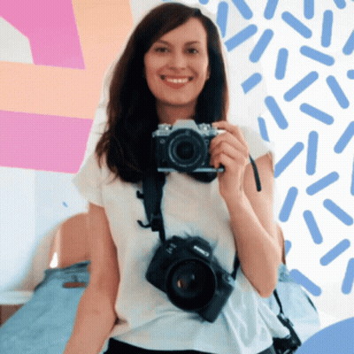 A Woman Is Smiling While Holding A Camera That Says Canon On It GIF
