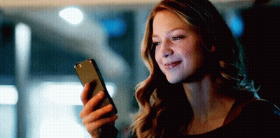 A Woman Is Smiling While Holding A Cell Phone In Her Hand . GIF