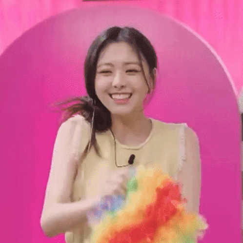 A Woman Is Smiling While Holding A Rainbow Colored Clown . GIF