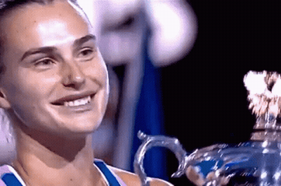 A Woman Is Smiling While Holding A Trophy In Her Hands . GIF