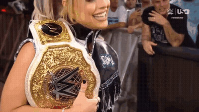 A Woman Is Smiling While Holding A Wrestling Championship Belt . GIF
