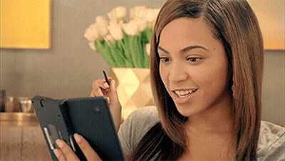 A Woman Is Smiling While Looking At A Tablet With A Pen In Her Hand GIF