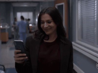 A Woman Is Smiling While Looking At Her Phone GIF