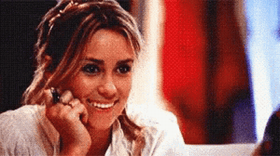 A Woman Is Smiling While Looking At Herself In A Mirror GIF