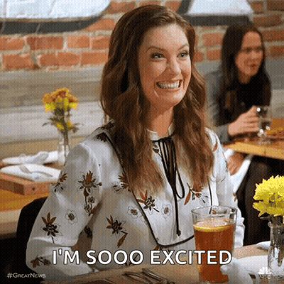 A Woman Is Smiling While Sitting At A Table With A Glass Of Beer And Says I 'M Sooo Excited . GIF