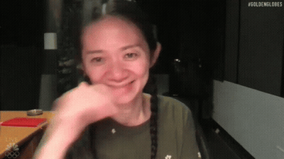 A Woman Is Smiling While Sitting At A Table With Her Hand On Her Face . GIF