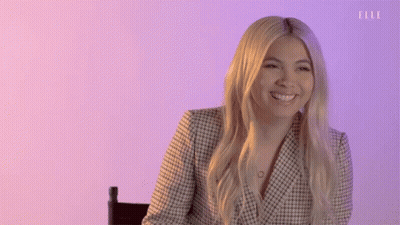 A Woman Is Smiling While Sitting In A Chair In Front Of A Purple Wall . GIF