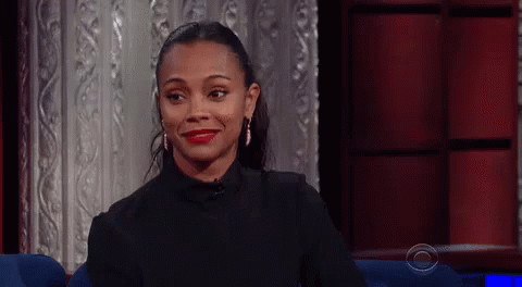 A Woman Is Smiling While Sitting In A Chair In Front Of A Red Curtain . GIF