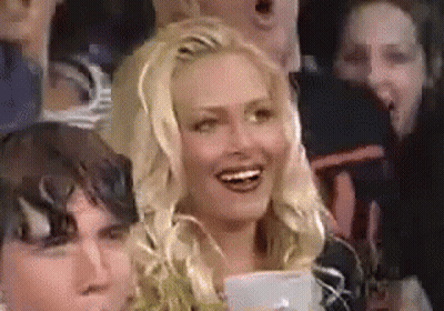 A Woman Is Smiling While Sitting In A Crowd . GIF