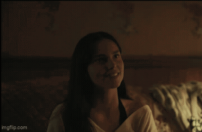 A Woman Is Smiling While Sitting On A Bed In A Dark Room GIF